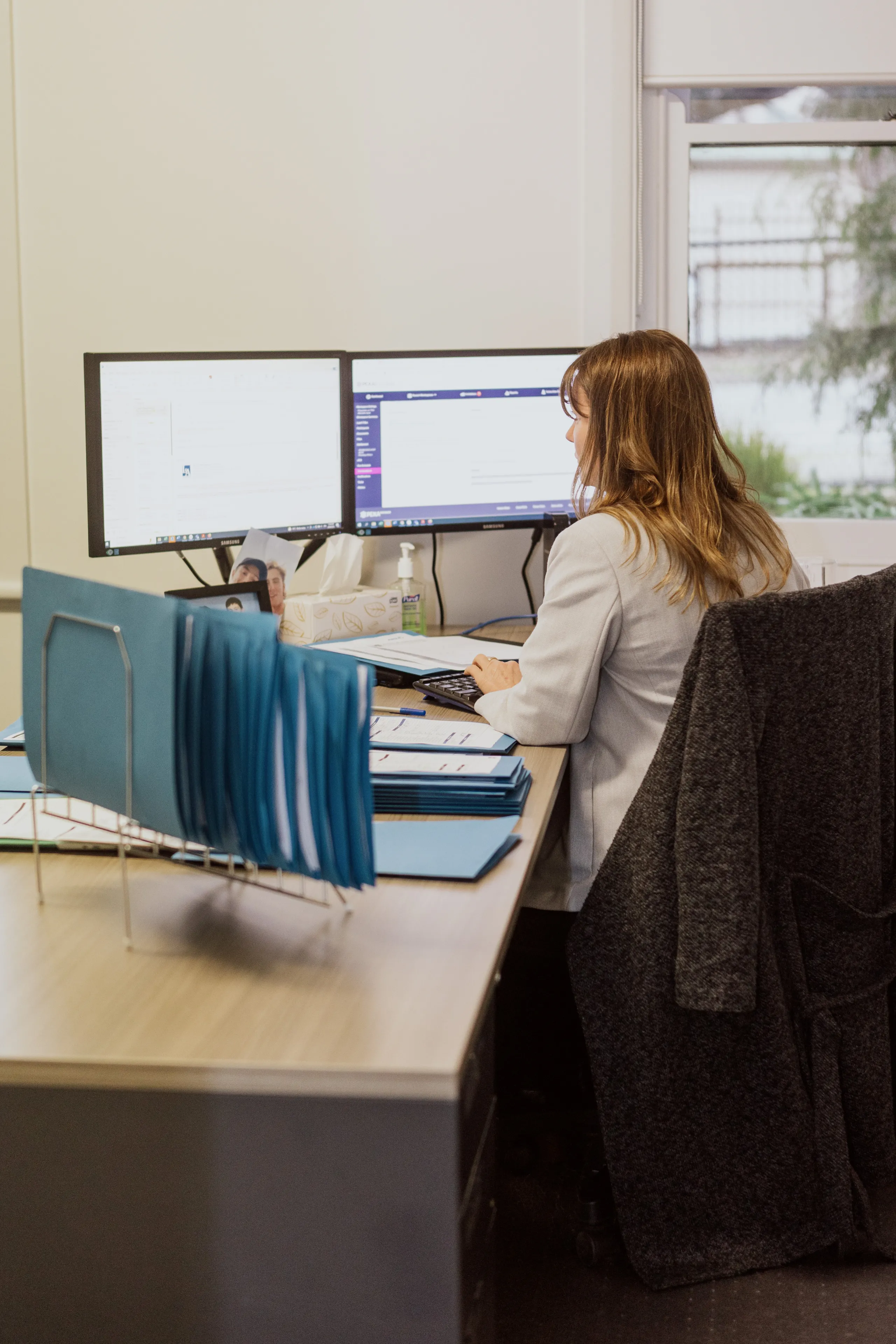 Team member working in front of a computer with blue folders beside her.